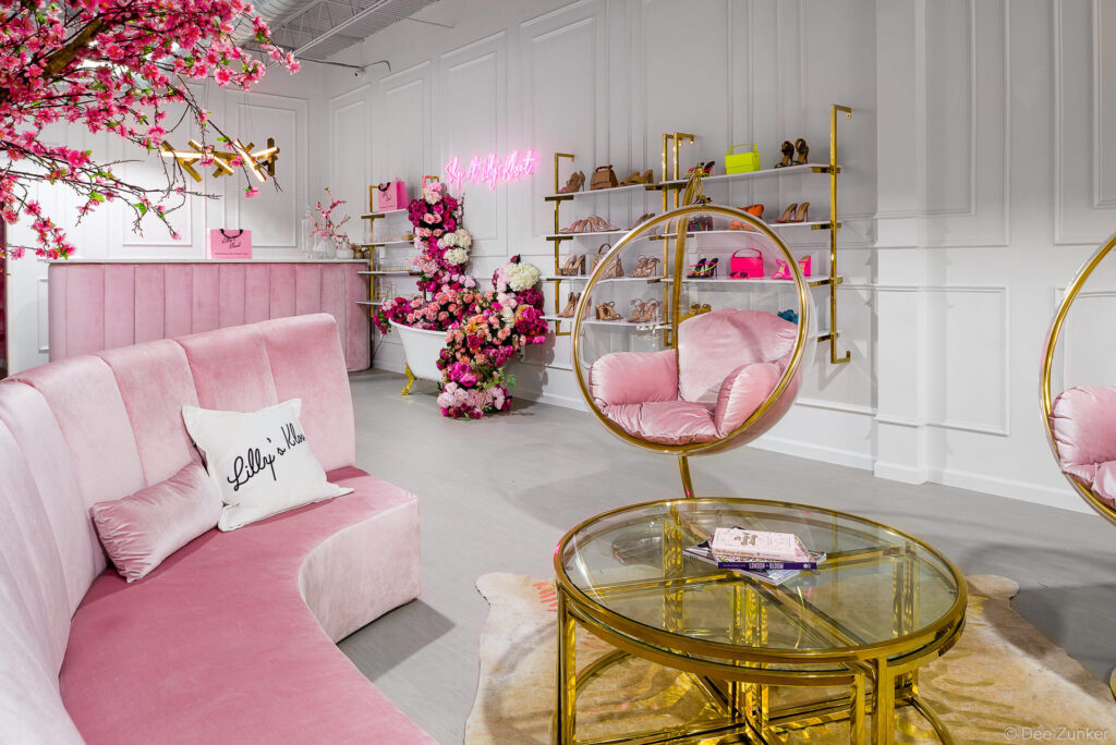 Luxurious pink velvet curved sofa, gold bubble chairs, floral bath display, and shoe shelves in a Houston boutique interior.