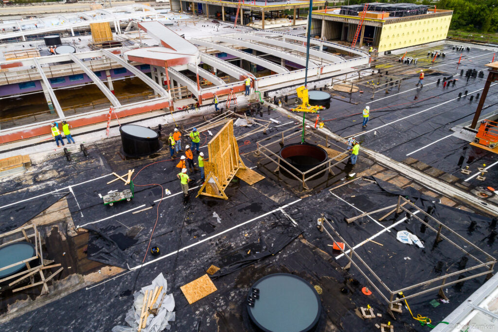 Aerial view of workers in hi-vis vests installing rooftop MEP penetrations and waterproofing membrane on Post HTX Houston rooftop construction site.
