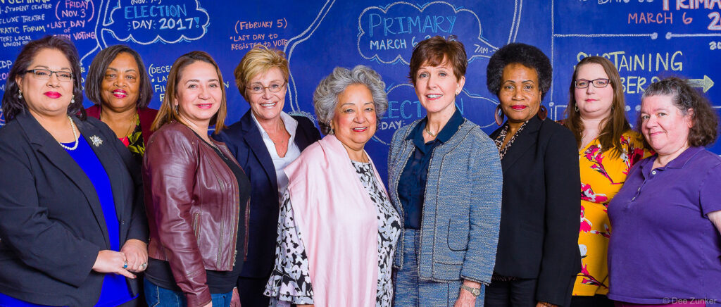 Group of nine professional women posing together at a corporate event in Heights Houston, diverse business group photo