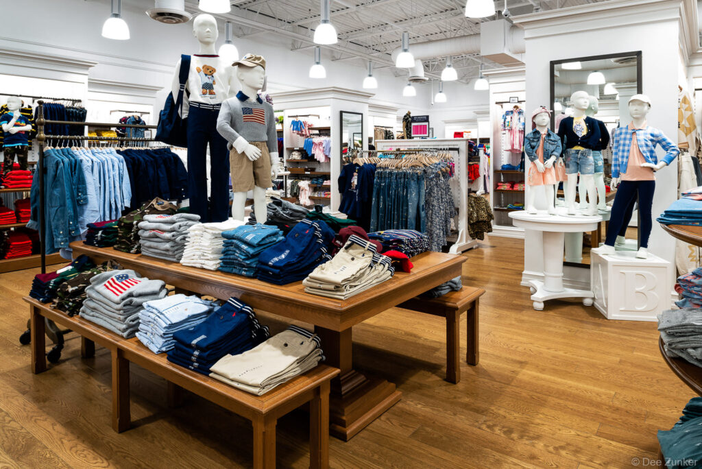 Bright children's clothing retail store interior with mannequins, folded apparel displays, and pendant lighting in Houston, TX.
