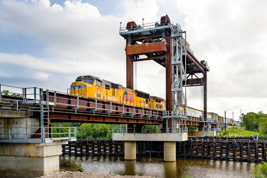 Yellow freight locomotive crossing the new San Bernard River railroad lift bridge over water in Texas