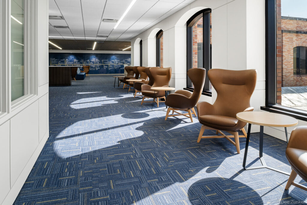 Sunlit lounge area with leather wingback chairs and blue patterned carpet inside a school library sixth floor interior