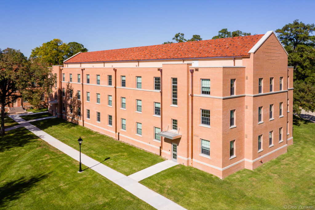 Aerial exterior view of a three-story red brick seminary building with terracotta roof on a landscaped Houston campus