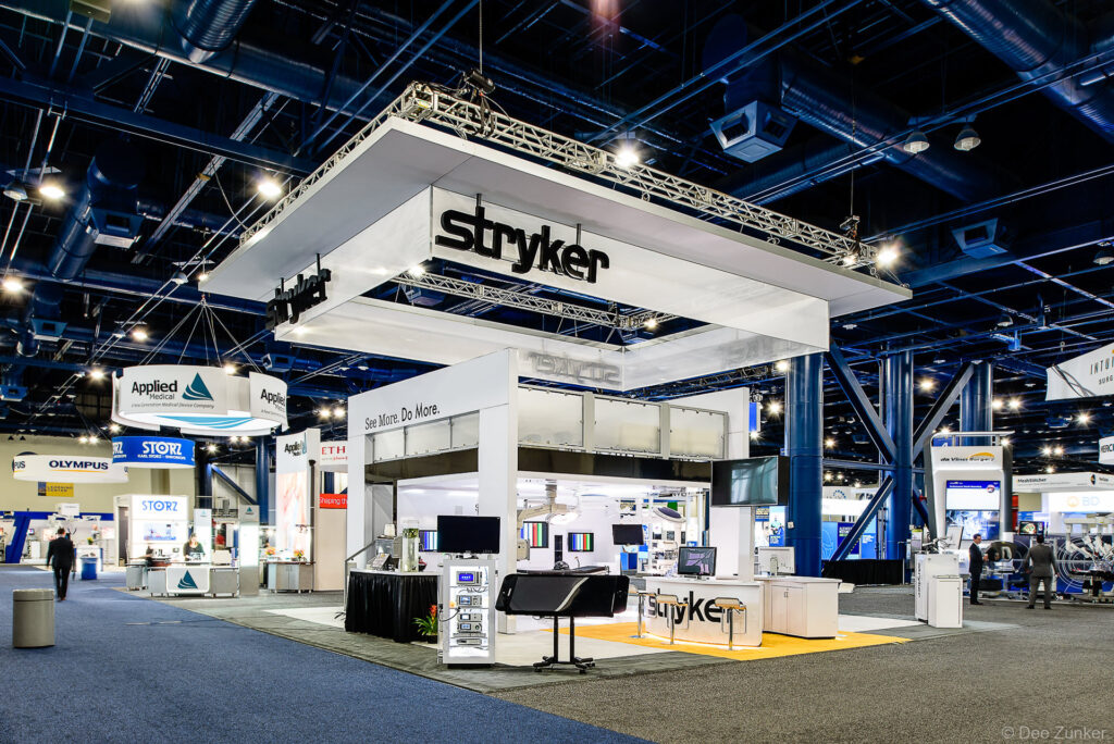 Large two-story Stryker medical equipment exhibit booth with overhead signage at a Houston convention center trade show, photographed by Dee Zunker Photography.