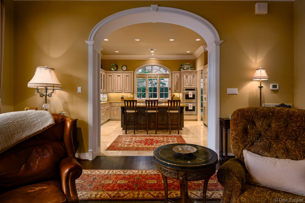 Elegant Houston home interior featuring white arched doorway connecting formal living room and kitchen with bar seating and warm gold walls.