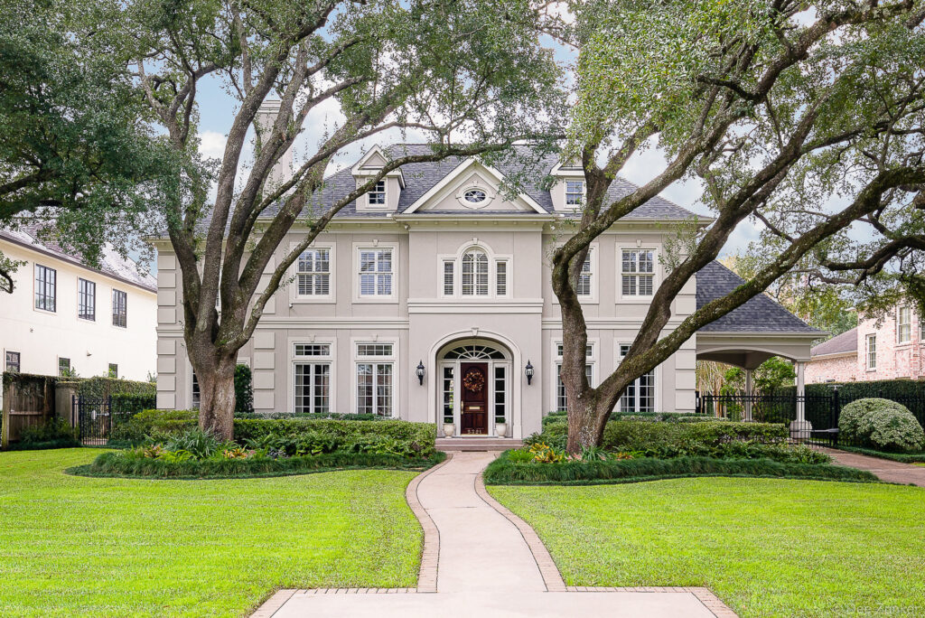 Grand two-story stucco estate on Sugar Hill Drive Houston with arched entry, mature oak trees, and manicured lawn.
