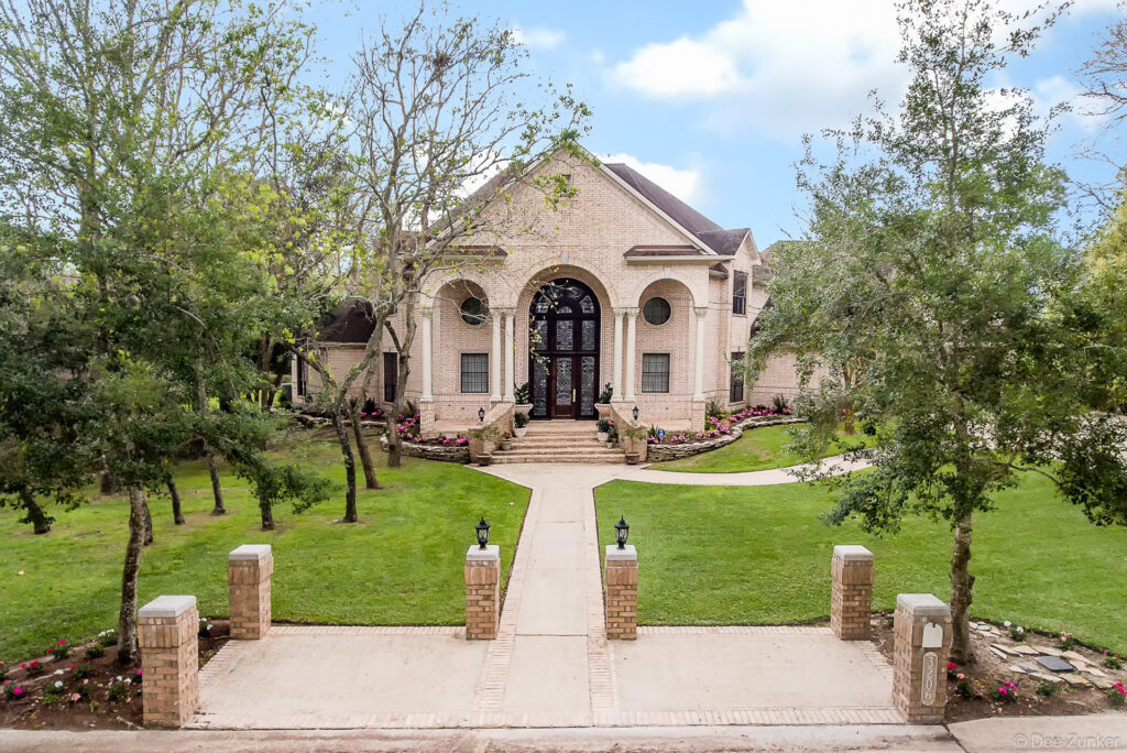 Grand brick luxury home exterior in Tanglewood Houston featuring arched portico entry columned facade and manicured front lawn