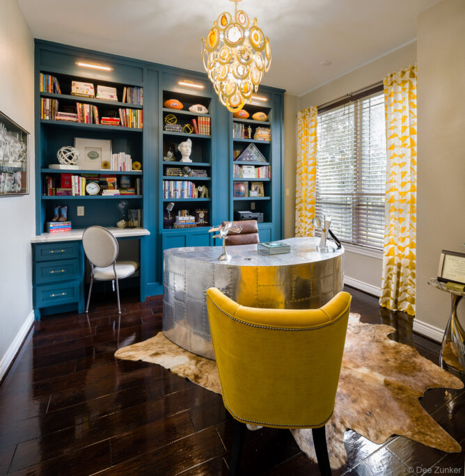 Eclectic Houston home office with teal built-in bookcases, riveted metal aviator desk, mustard yellow accent chair, and agate chandelier.
