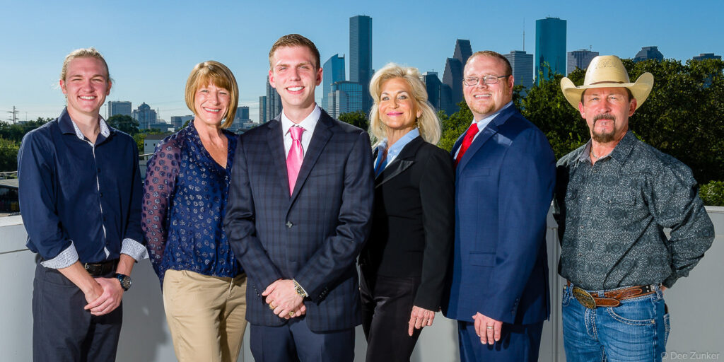 Six corporate team members smiling together on a rooftop with the Houston skyline in the background