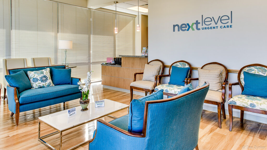 Bright urgent care waiting room with blue upholstered chairs, wood floors, reception desk, and modern pendant lighting in Sugar Land Texas