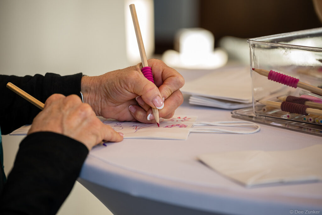 Close-up of hands using a colored pencil with ergonomic grip to decorate a small gift bag at a Houston charity conference event.