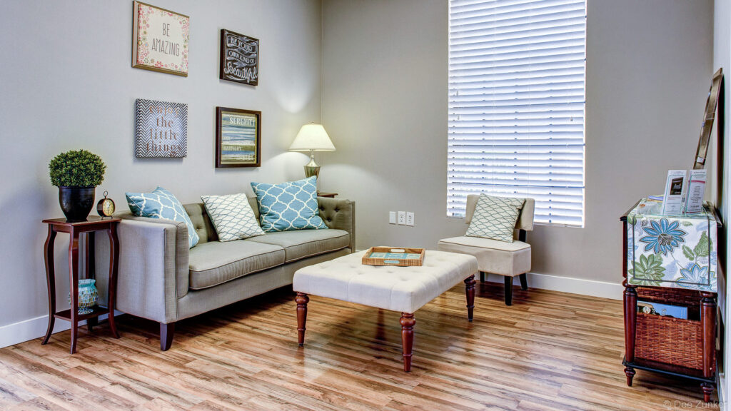 Bright wellness center waiting room in Sugar Land TX featuring neutral sofa teal accent pillows ottoman and motivational wall art