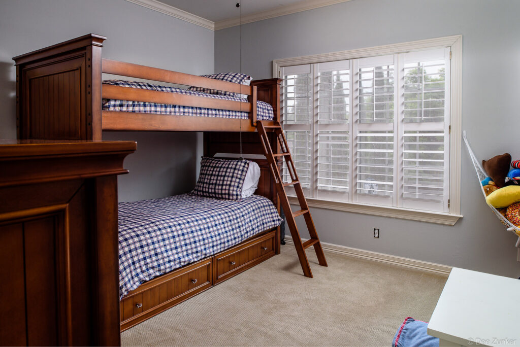 Cherry wood bunk beds with blue plaid bedding in a West University Houston home, featuring plantation shutters and built-in storage drawers.